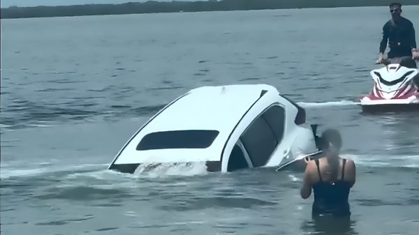 Vrouw kijkt pijnlijk toe hoe haar auto langzaam de zee in wordt getrokken